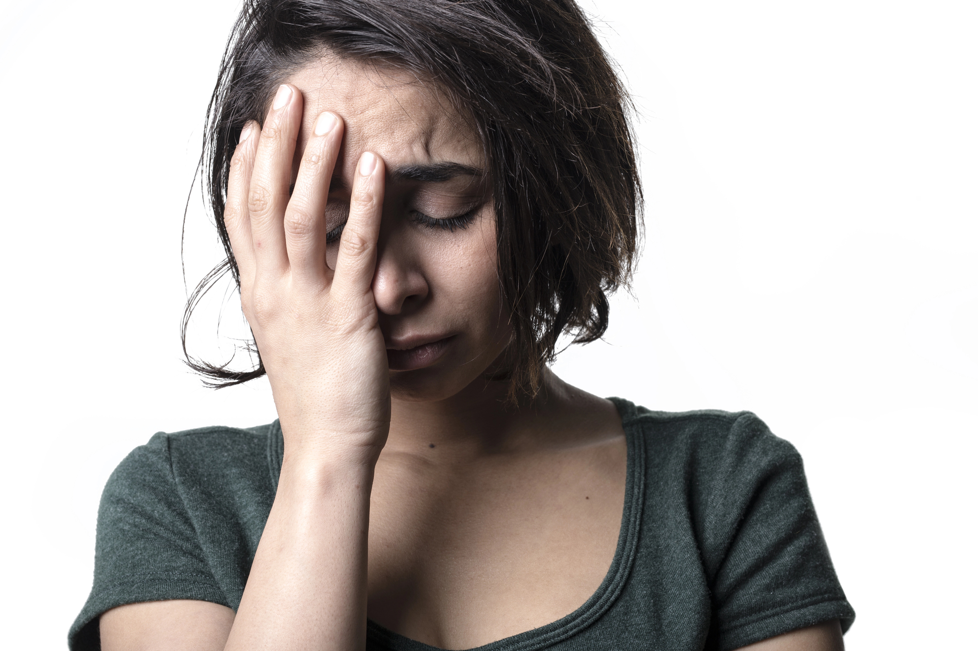 A woman with short dark hair is holding her hand to her forehead, eyes closed, and appears upset or stressed. She is wearing a dark green top against a plain white background.