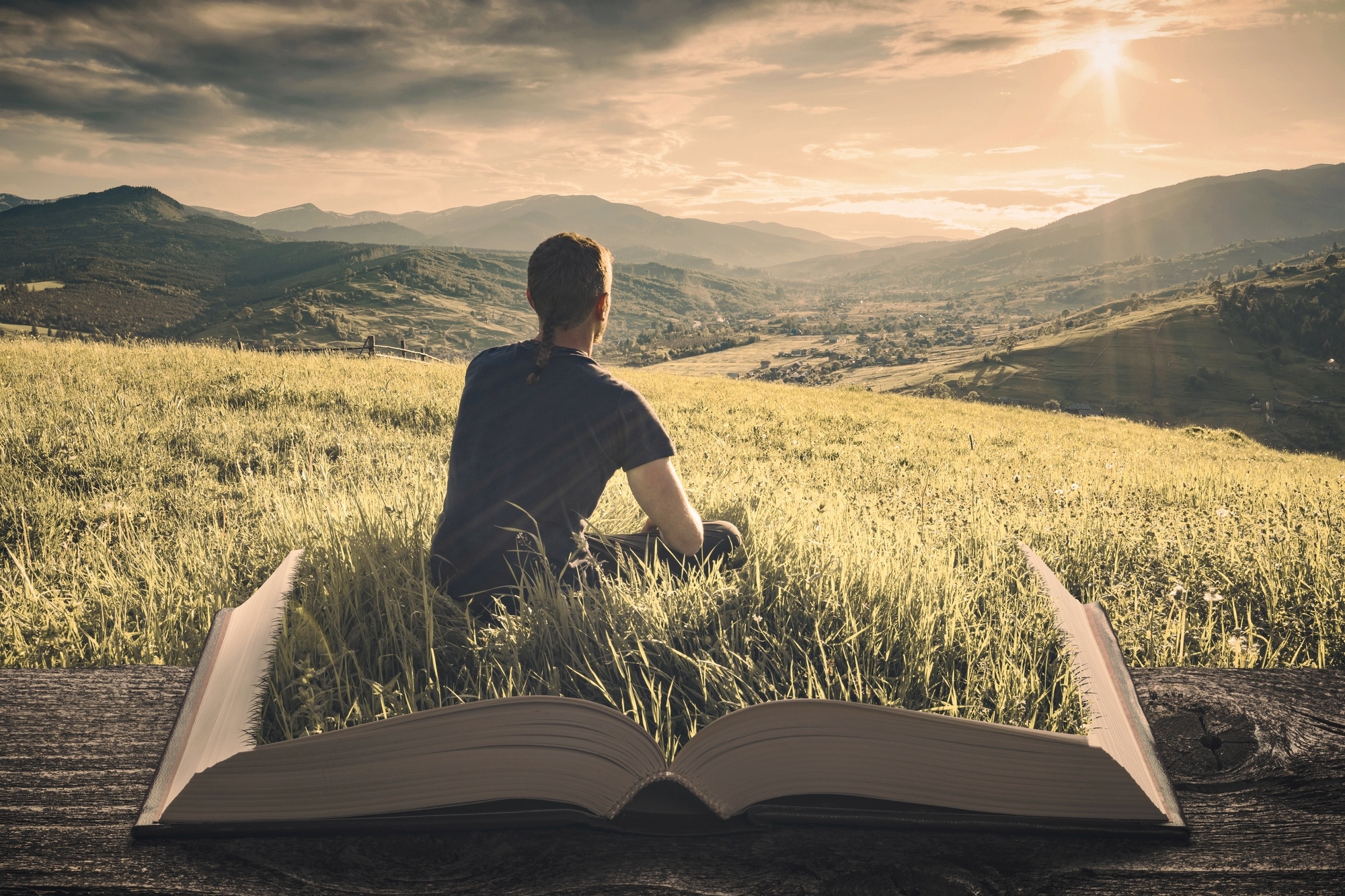 A person sits on an open book that seamlessly blends into a grassy landscape. They face a vast valley with distant mountains under a dramatic sunset sky, symbolizing the connection between nature and literature.