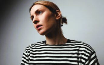 A person with light brown hair is looking to the side against a plain background. They are wearing a black and white striped shirt.