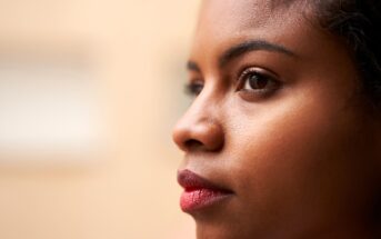 Close-up profile view of a person with a contemplative expression, looking toward the right. Features include brown eyes, smooth skin, and dark hair. The background is softly blurred, enhancing focus on the face.