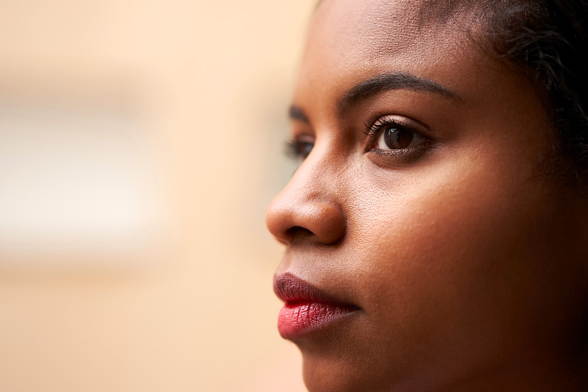 Close-up profile view of a person with a contemplative expression, looking toward the right. Features include brown eyes, smooth skin, and dark hair. The background is softly blurred, enhancing focus on the face.