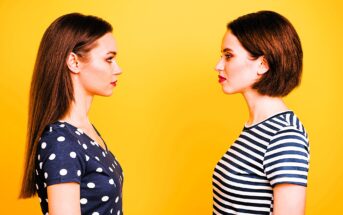 Two women facing each other against a bright yellow background. The woman on the left has long, straight hair and wears a polka dot top, while the woman on the right has a short bob haircut and wears a striped top.