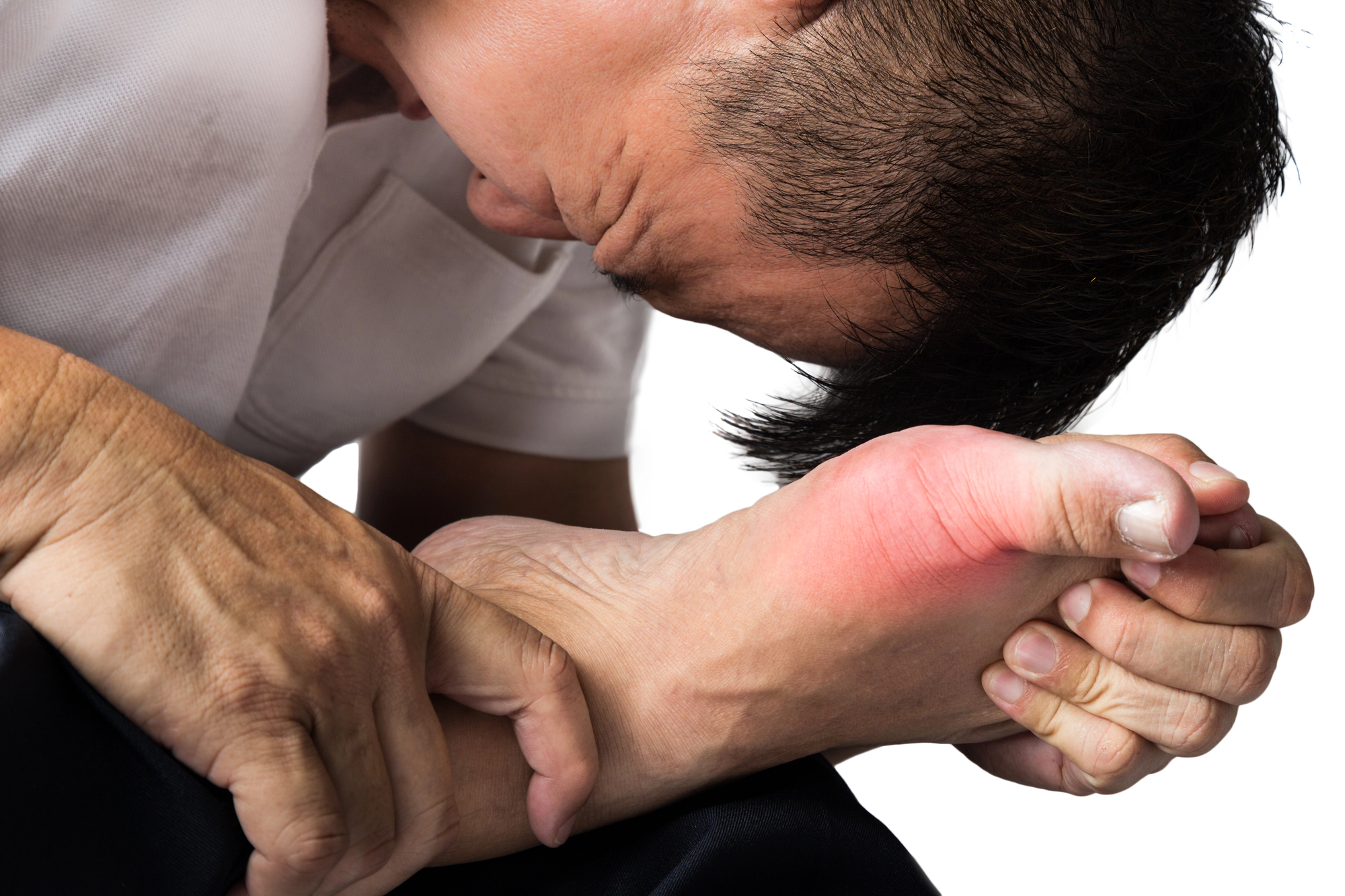 A person holds their foot, showing a red, inflamed area near the big toe. They appear in discomfort, suggesting pain or possible gout. The background is bright and neutral.